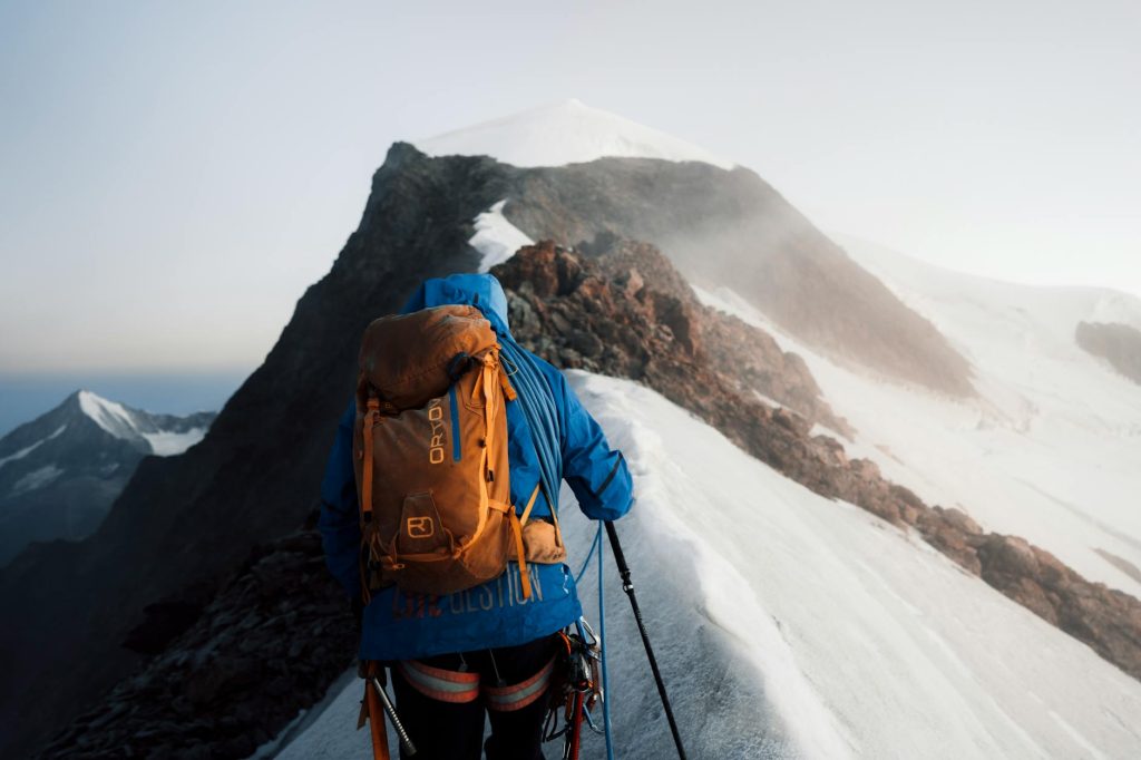 Mountaineer in blue gear climbs snowy peak, embracing the adventure.