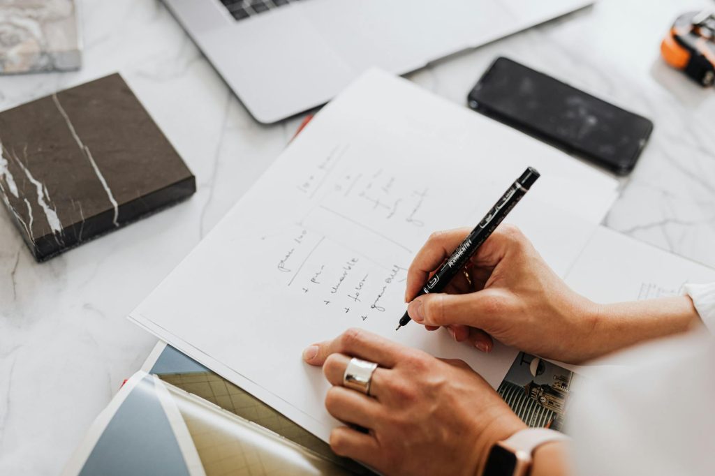 Hands writing ideas in a notebook, symbolizing creativity and productivity in an office setting.