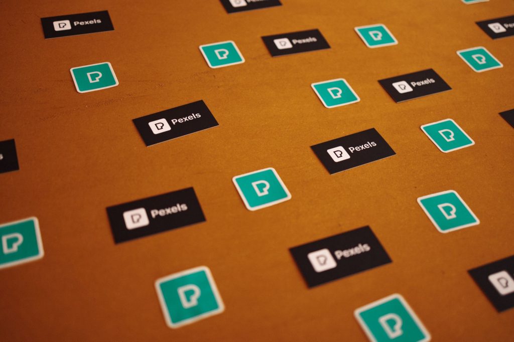 Pexels logos and stickers scattered on a brown background in a creative pattern.